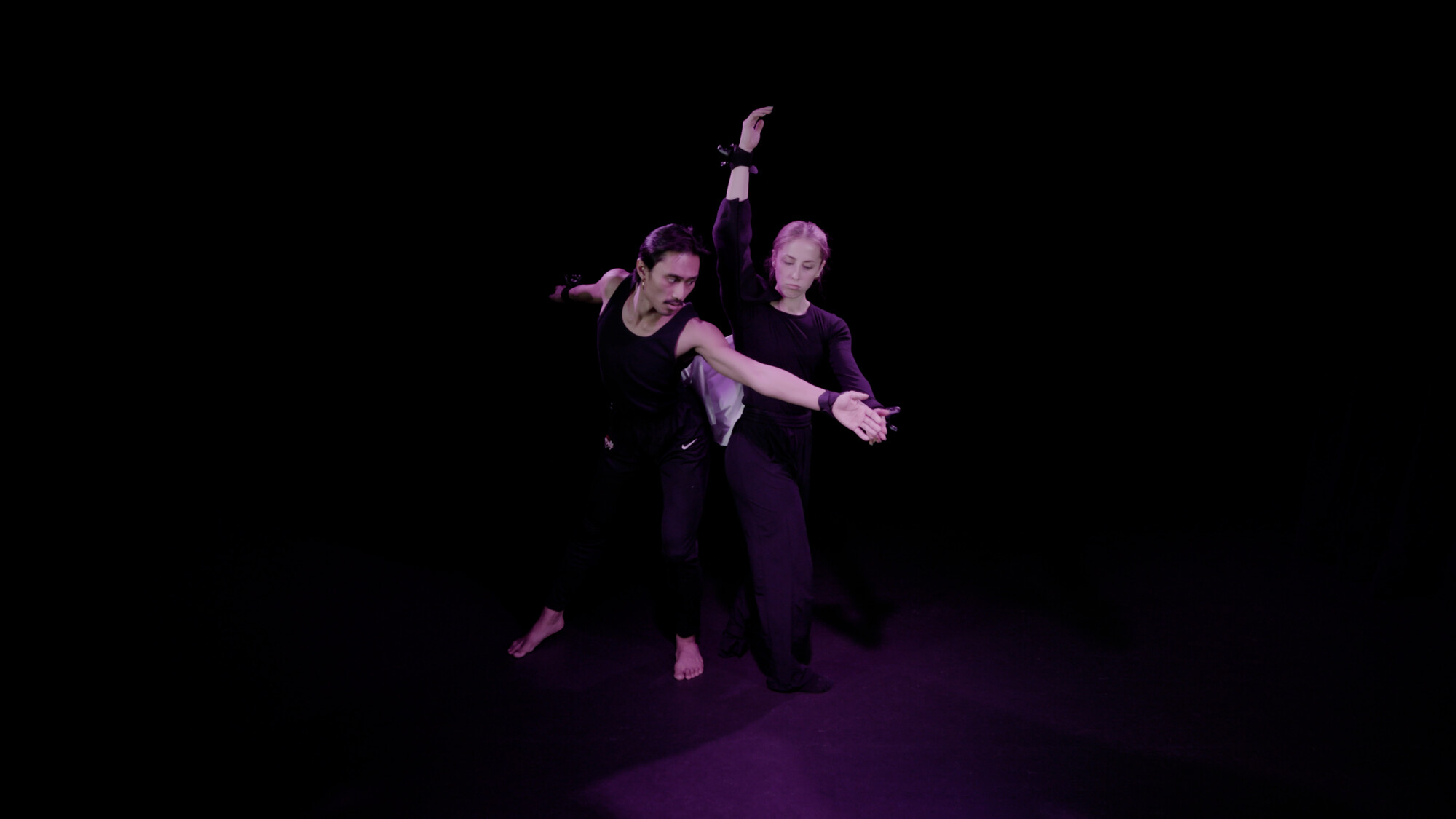 Two actors in wearing black perform in front of a black backround.