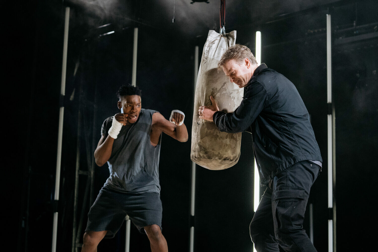 Two actors stand on a set that is staged to look like a boxing gym.