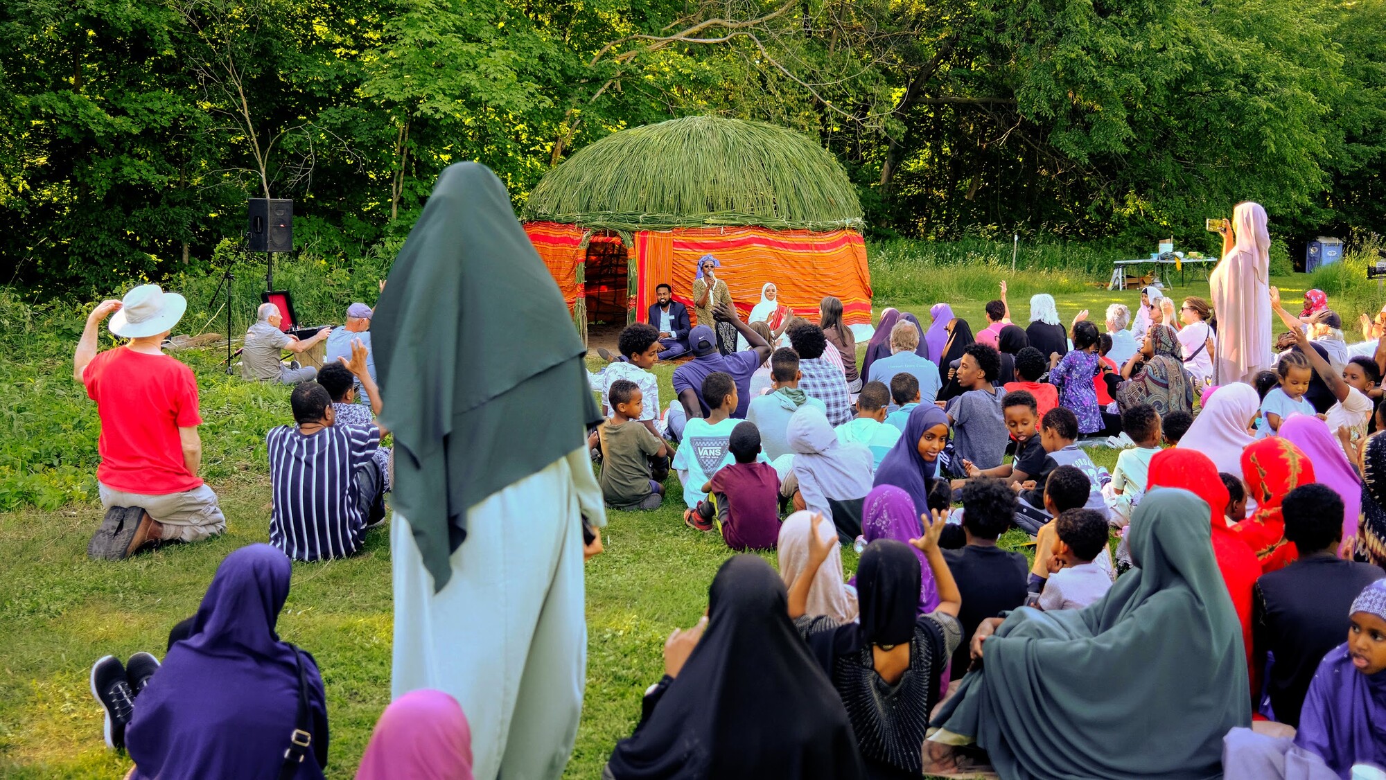 Performers and audience members gather in a park.