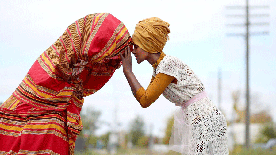 A woman leans her head against a figure wrapped in a colorful blanket