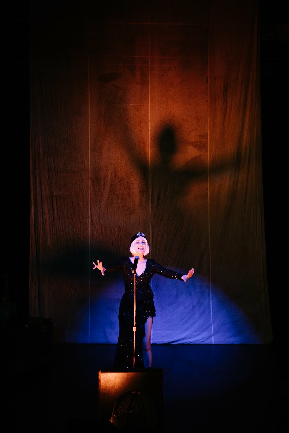 An actor sings into a microphone under a blue spotlight.