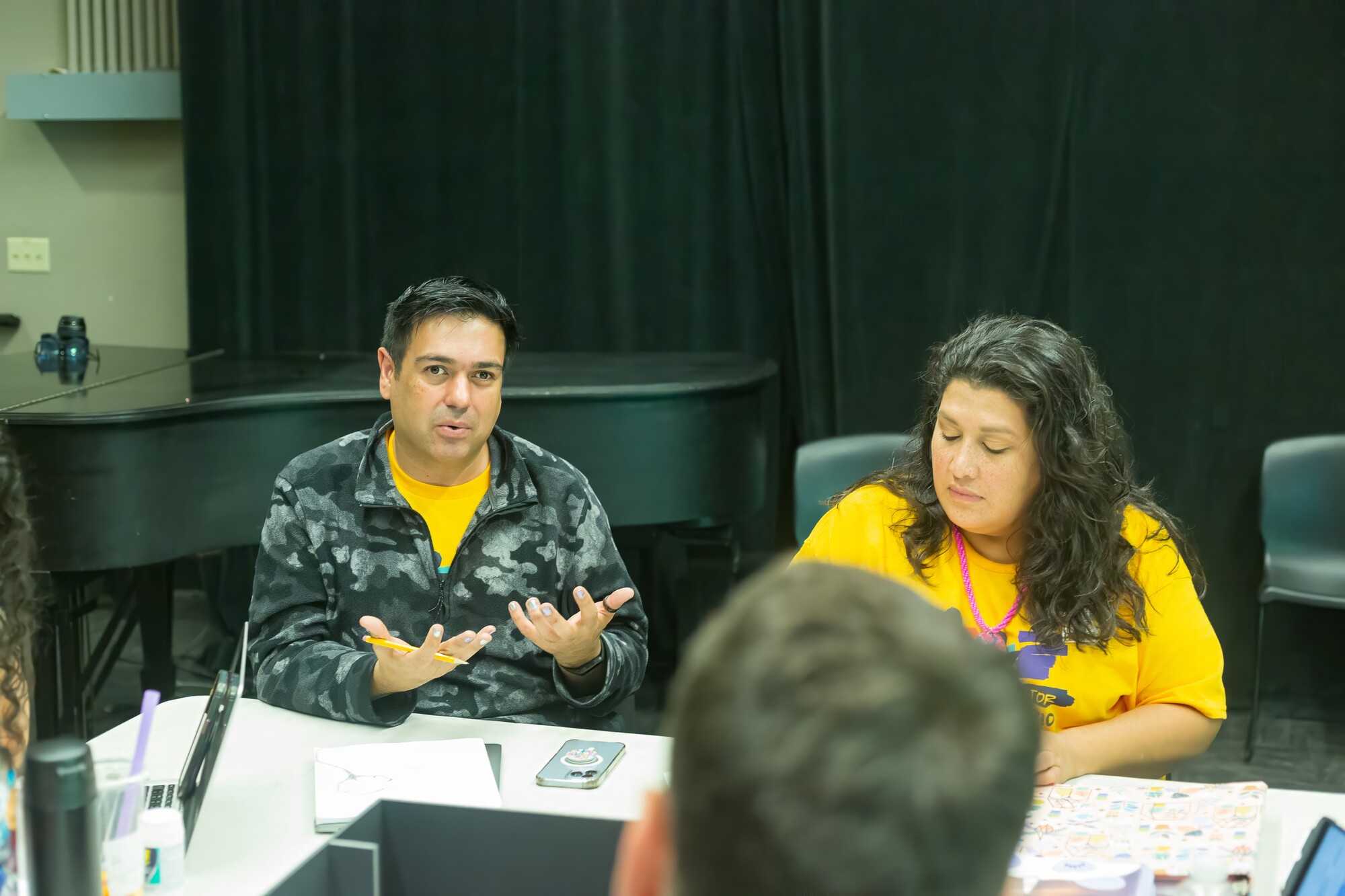 Two artists in yellow T-shirts work together at a table.