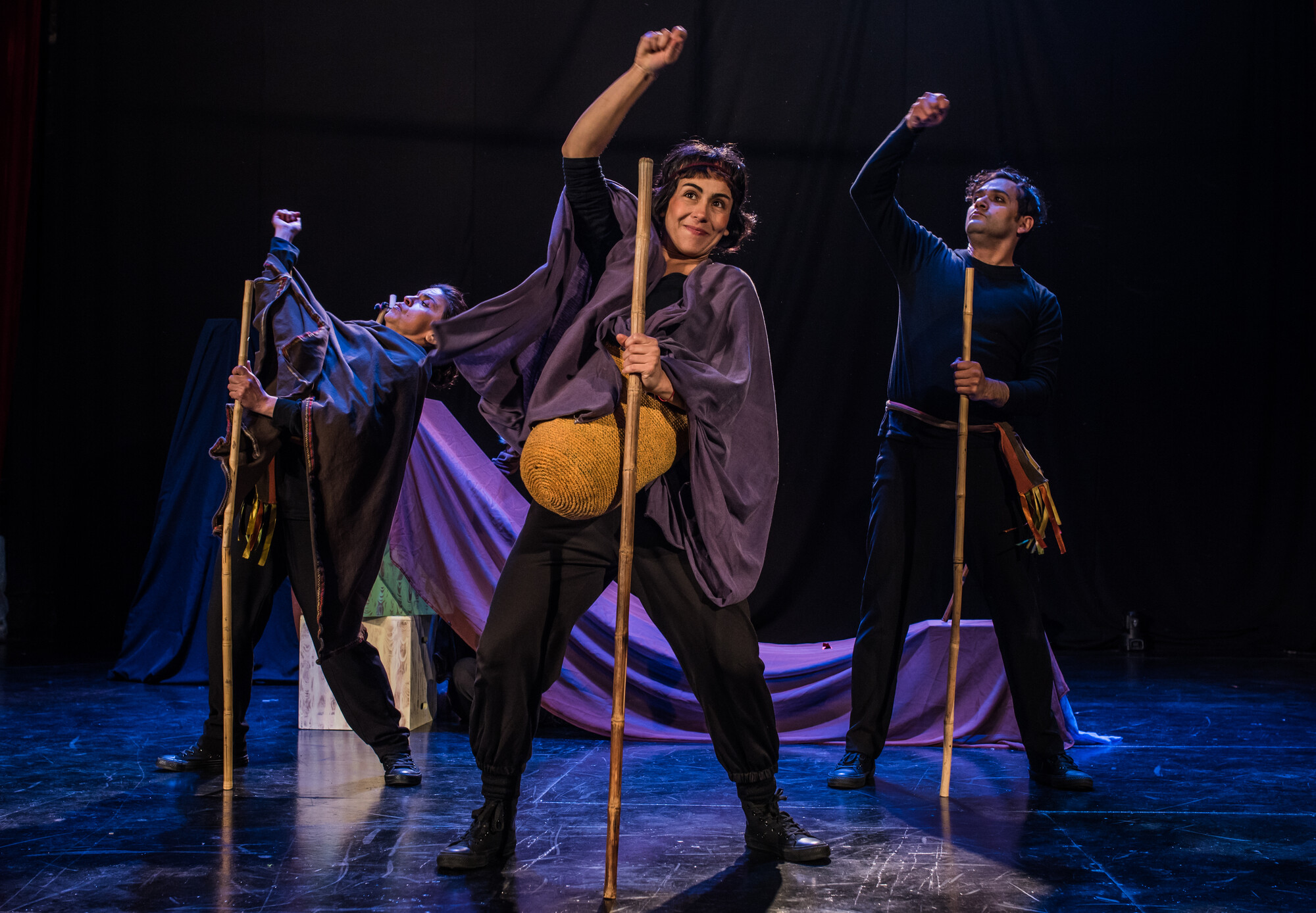 Three actors  perform on stage with wooden props.