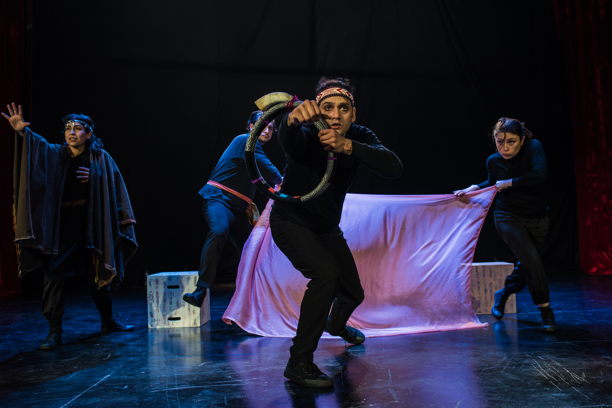 Four actors wearing black perform on stage with a white sheet.