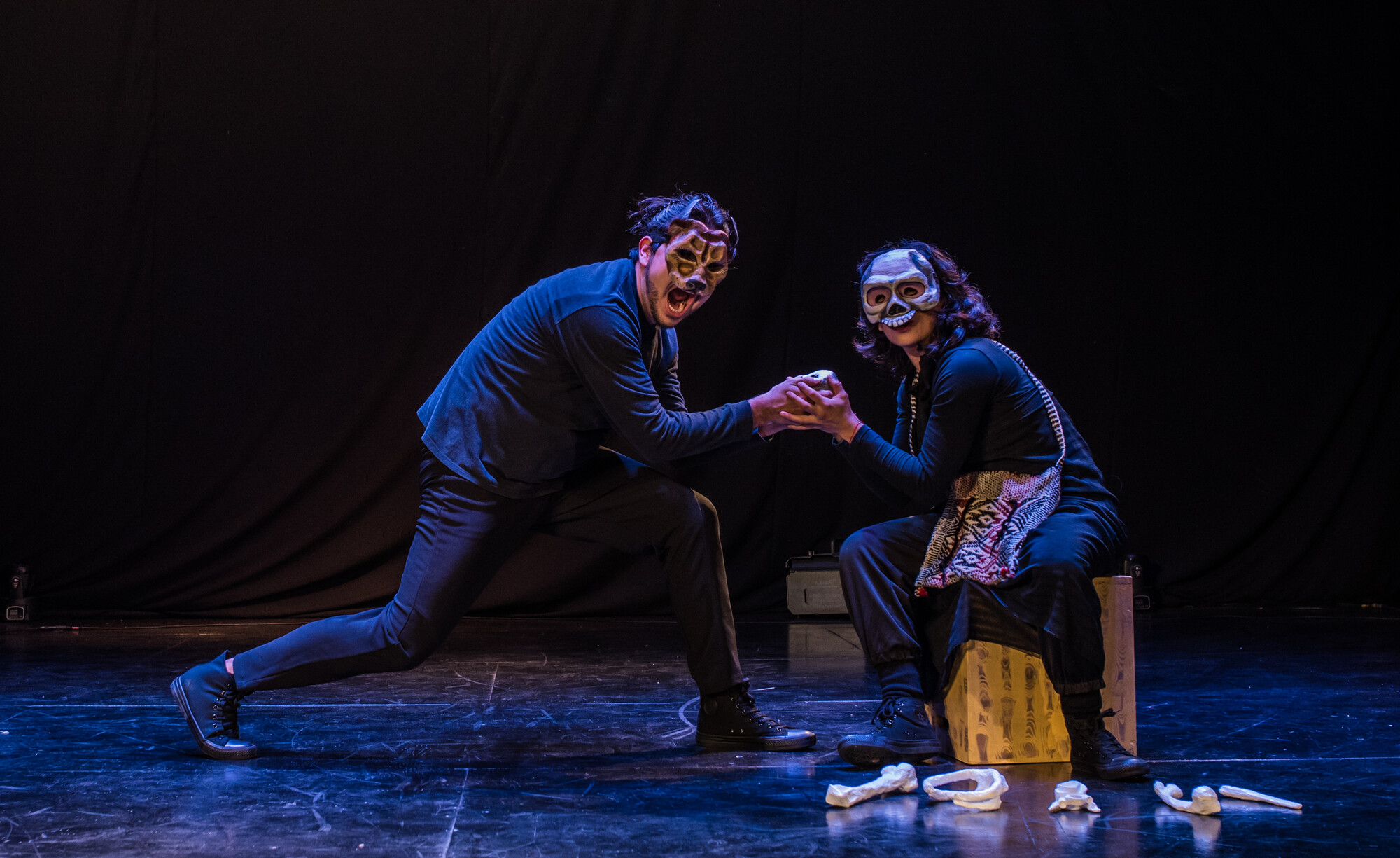 Two actors wearing masks perform on stage.