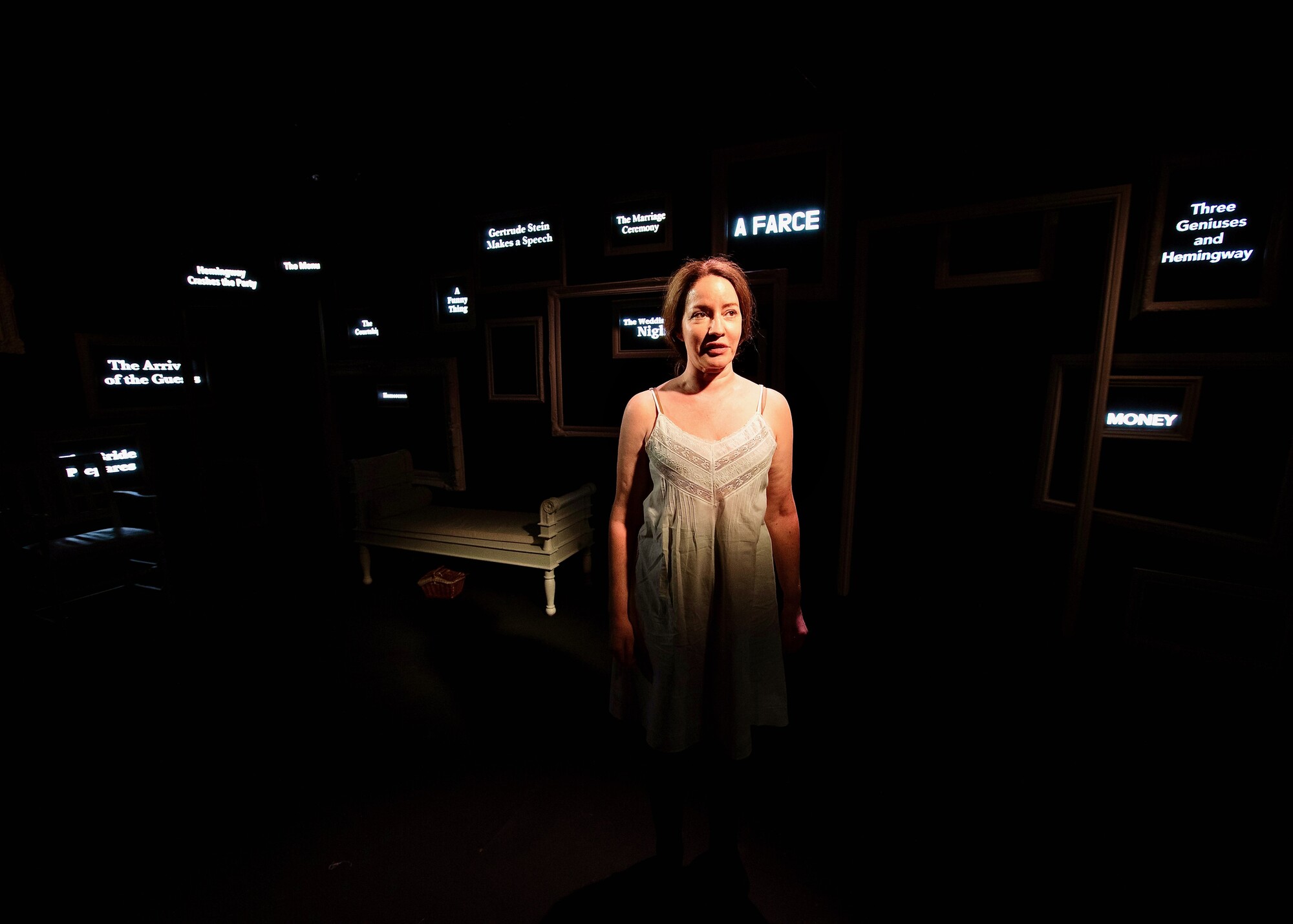 A woman wearing white stands on stage in front of projections of different words.