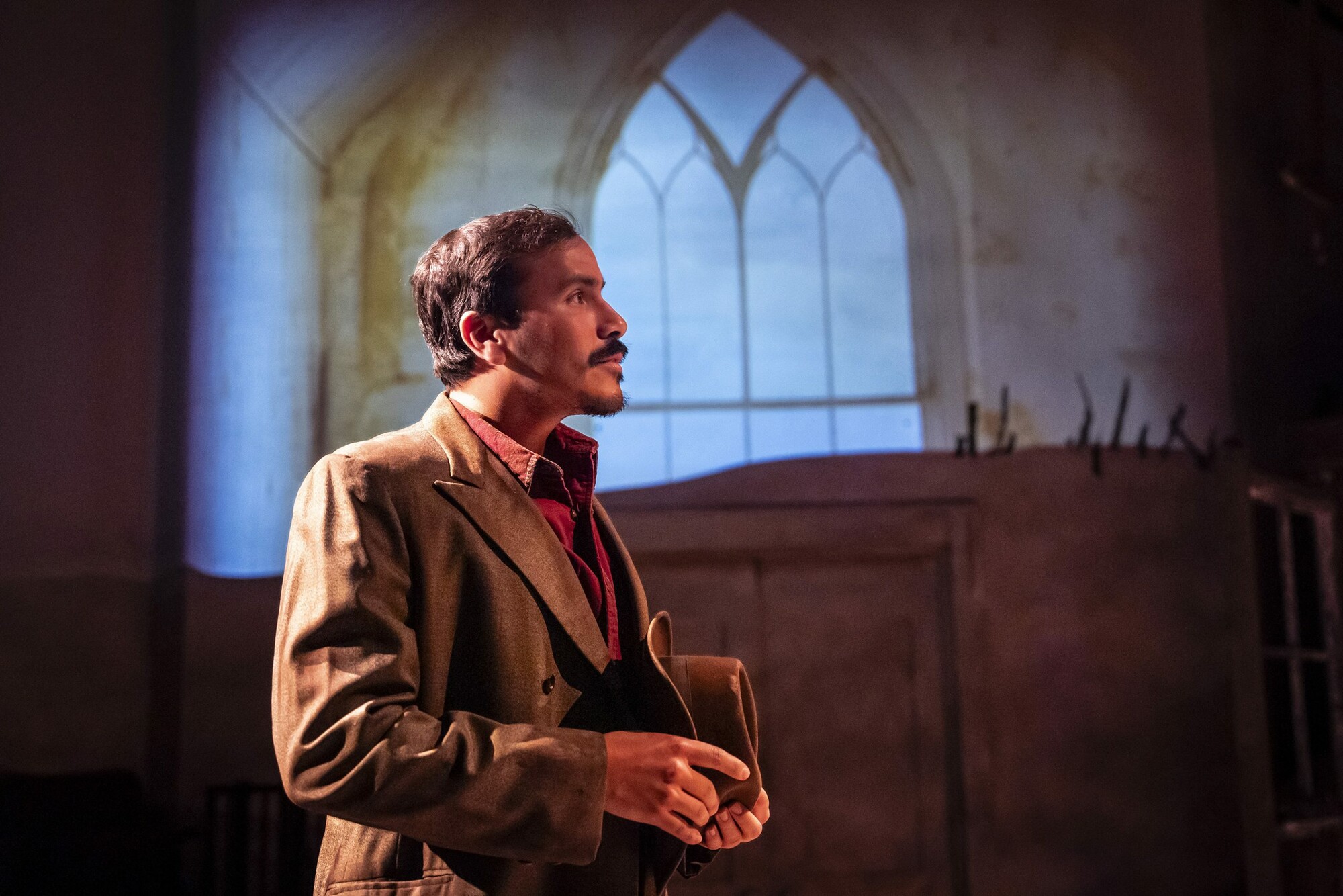 An Actor stands on stage in front of a backdrop of a church.