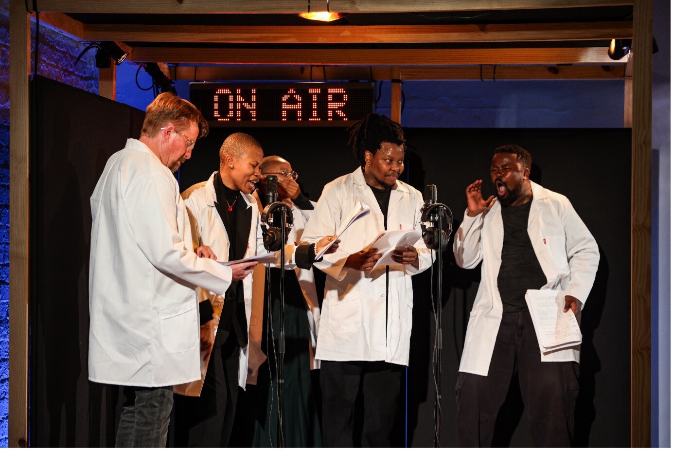 A group of artists in white coats stand in a recording booth.