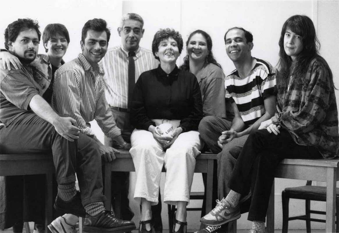 A black and white photograph of a group of writers and artists sitting on desks.