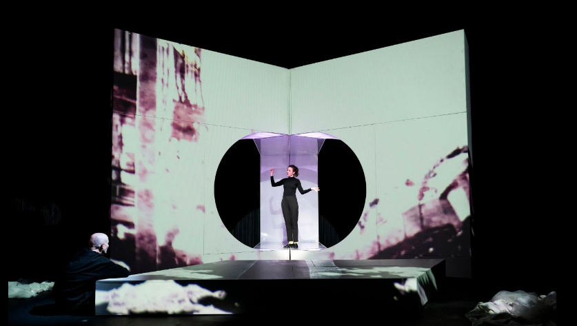 An actor performs in front of a large abstract projection onstage.